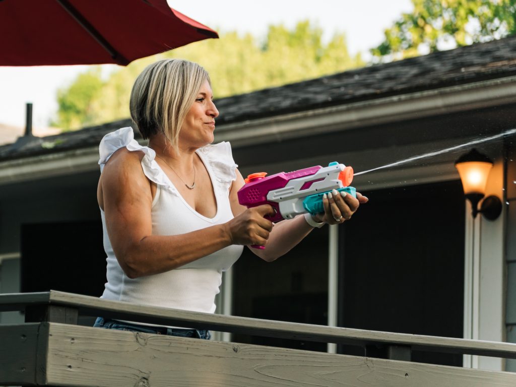 Grand Island Mom squirting water gun at her kids off the porch